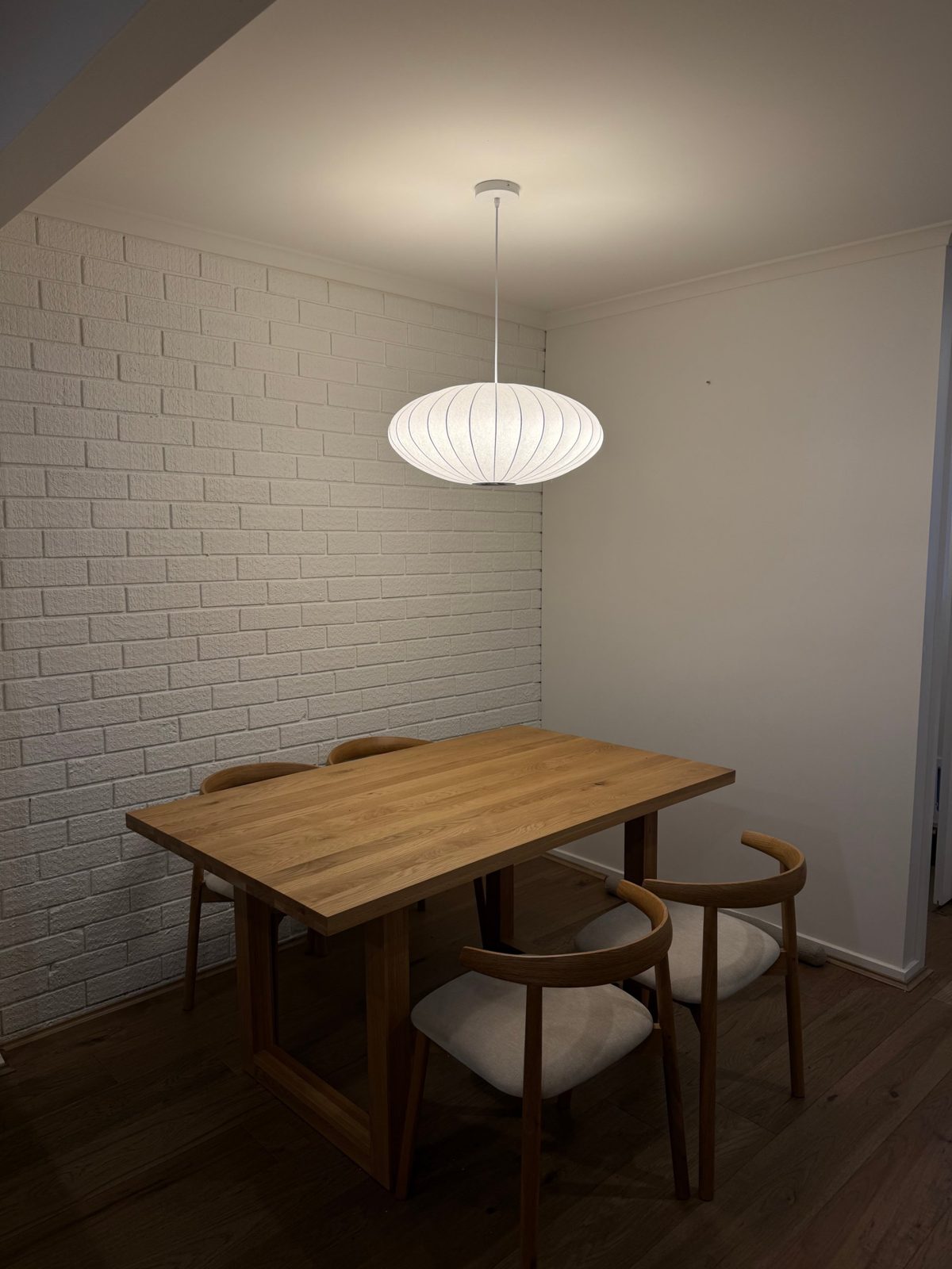White pendant light hanging over a timber dining table