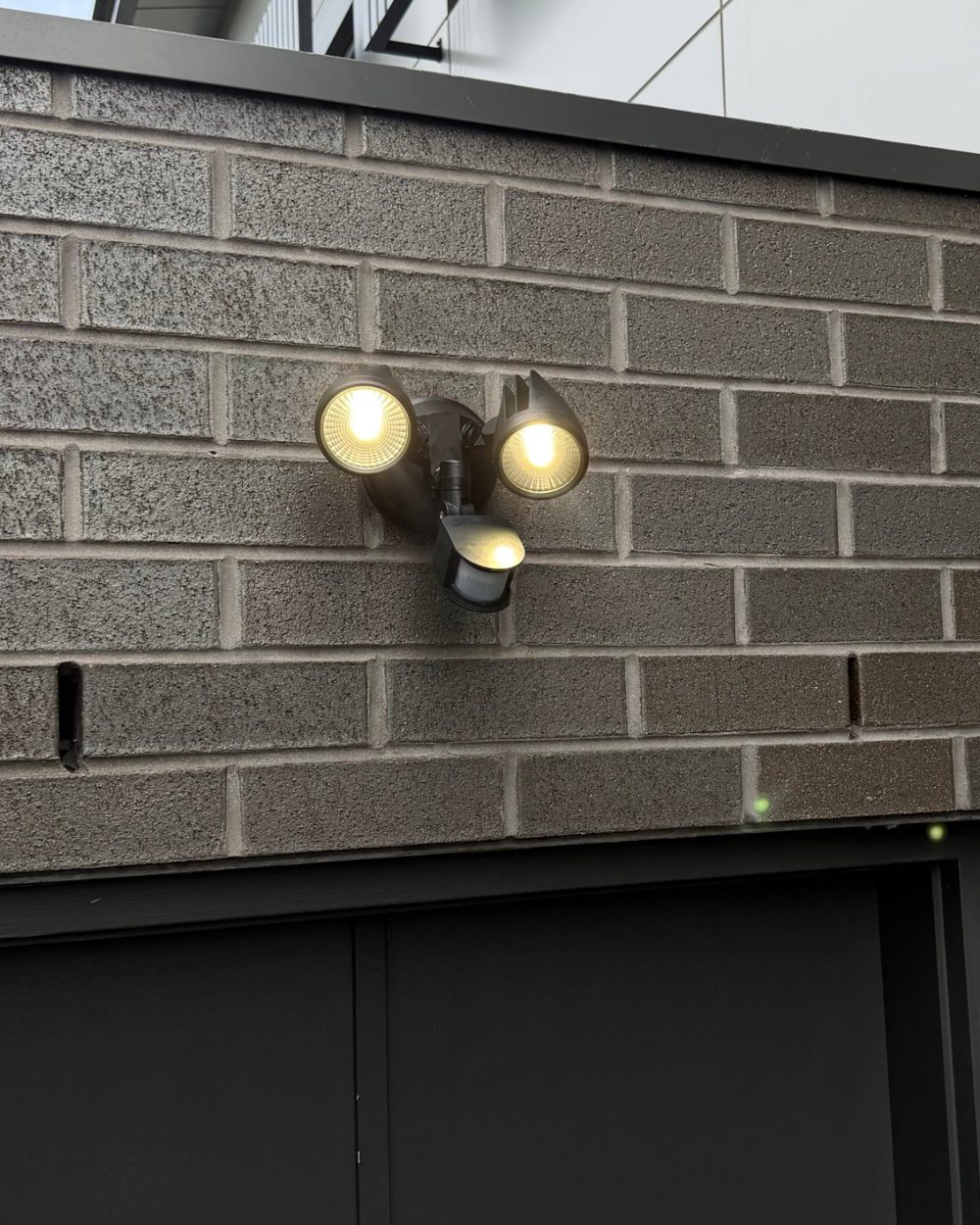 Twin LED spotlight with motion sensor mounted on an exterior brick wall